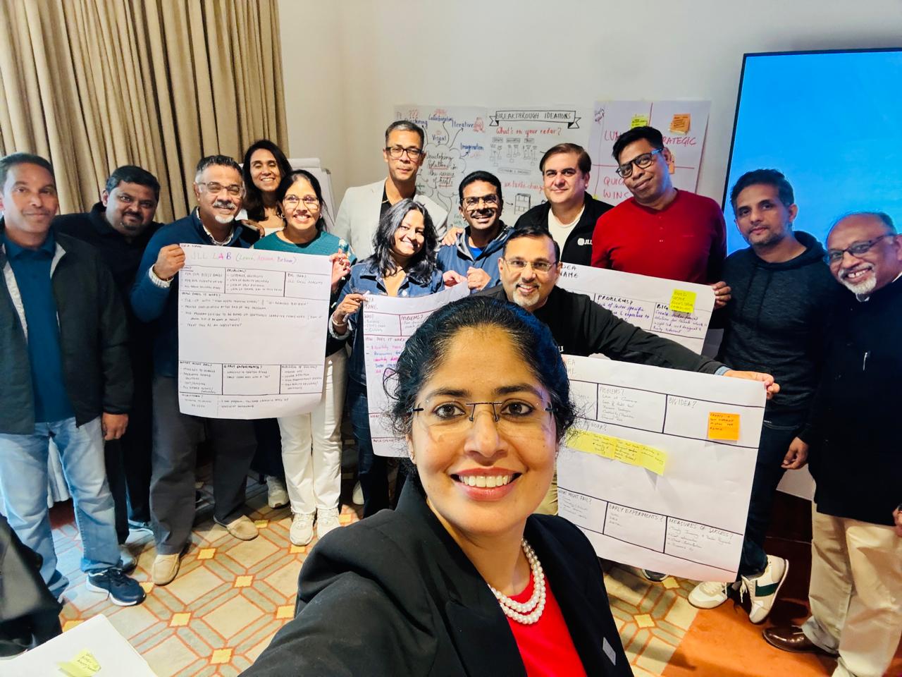 Shalu Manan with JLL leadership workshop participants holding Learn Assess Believe flipchart outputs